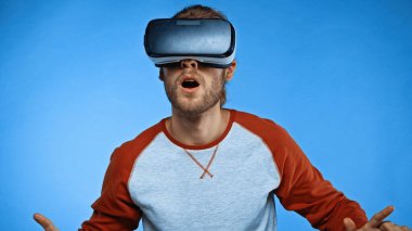shocked young man in virtual reality headset on blue  clipart