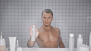 Banyoda deodorant şişesi tutan kaslı bir adam. 