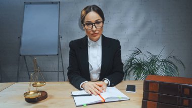 Sigorta acentesi bilgisayarın, akıllı telefonun ve kitapların yanındaki kameraya bakıyor. 