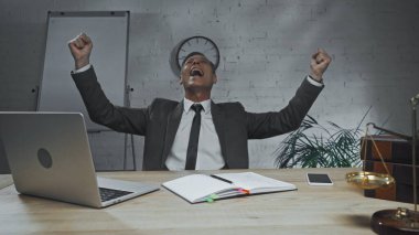 Heyecanlı sigorta acentesi, masanın yanında el kol hareketi ve not defteri gösteriyor. 