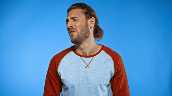 Молодой бородатый человек чувствует отвратительный запах на голубом