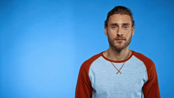 bearded young man looking at camera on blue background 