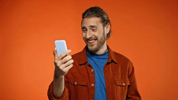 Fröhlicher Mann Blickt Auf Smartphone Orange — Stockfoto