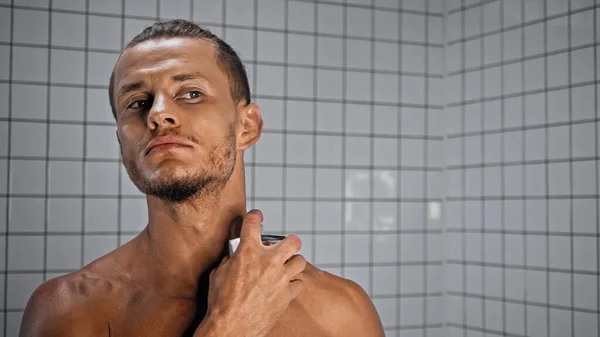 shirtless young man spraying perfume in bathroom