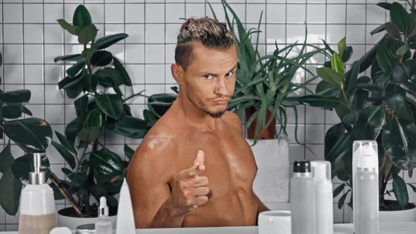 年轻的赤身裸体男子在浴室里用手指指尖看着绿色植物旁边的相机 背景模糊不清 — 图库照片