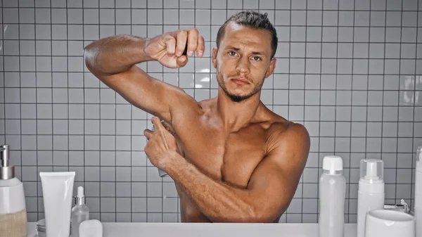 Hombre Sin Camisa Rociando Desodorante Cerca Botellas Baño Sobre Fondo — Foto de Stock