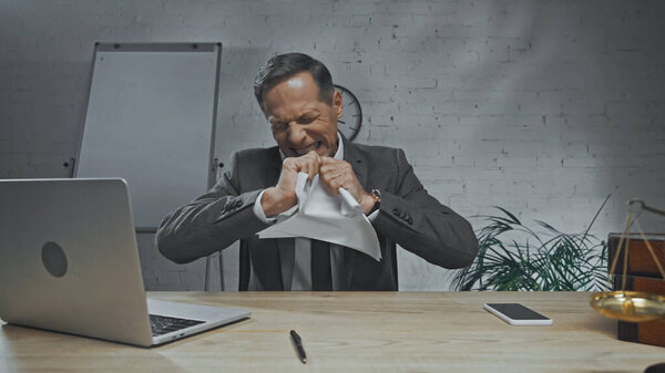 Angry insurance agent tearing papers near devices and scales on blurred foreground 