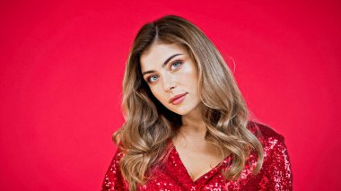 Mavi gözlü ve kıvırcık saçlı bir kadın kırmızı kameraya bakıyor.