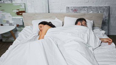 young man and woman sleeping back to back under white blanket clipart
