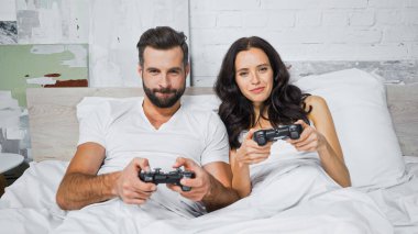 KYIV, UKRAINE - 26 Ocak 2021: yatak odasında joystickli konsantre çift oyunları