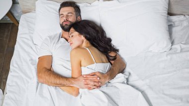 Genç bir çiftin evde uyurken kucaklaşması.