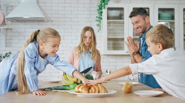 Çocuklar anne babalarının yanına kruvasan götürüyorlar mutfakta bulanık ön planda. 
