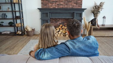 Back view of husband embracing wife near fireplace on blurred background at home  clipart