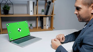 Bulanık ön planda oturan iş adamının yanındaki yeşil ekranlı dizüstü bilgisayar. 