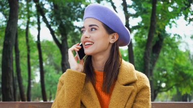 Sonbahar parkında cep telefonundan arayan mutlu, şık bir kadın.