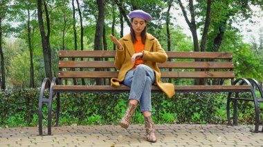 gücenmiş kadın sonbahar parkında bankta beklerken zamanı kontrol ediyor