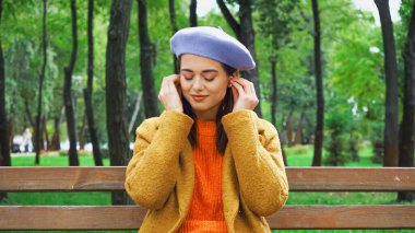 Parkta bankta müzik dinlerken hava telefonlarını ayarlayan neşeli kadın. 