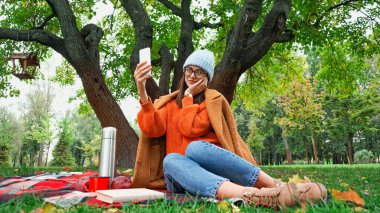 Gülümseyen kadın parkta piknik yaparken yüzüne dokunuyor.