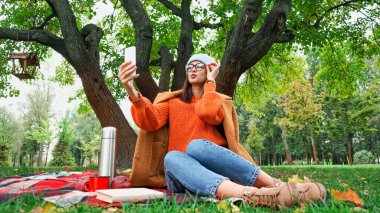 Parkta akıllı telefondan selfie çekerken gözlük takan şık bir kadın.