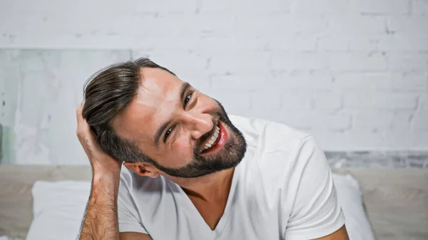 Hombre Positivo Tocando Pelo Mientras Sonríe Cámara Dormitorio —  Fotos de Stock