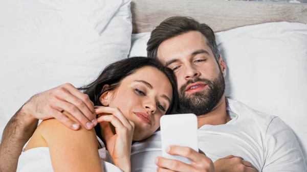 Man Met Baard Met Mobiele Telefoon Omarmen Glimlachende Vrouw Bed — Stockfoto