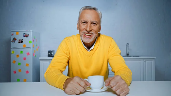 Lächelnder Älterer Mann Sitzt Neben Tasse Auf Küchentisch — Stockfoto