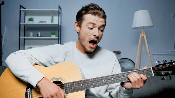 Genç Adam Akustik Gitar Çalıyor Evde Şarkı Söylüyor — Stok fotoğraf