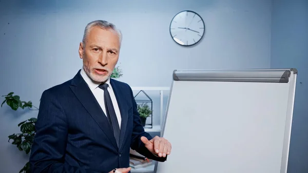 Elderly businessman talking at camera near flipchart during video call