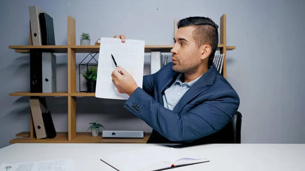 Geschäftsmann Zeigt Mit Stift Auf Papier Neben Notizbuch Auf Tisch — Stockfoto