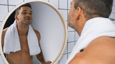 Gülümseyen üstsüz adam banyoda aynaya bakıyor, ön planda bulanıklık var