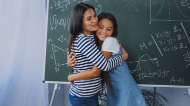 Mutlu anne ve kız matematik formülleriyle karatahtanın yanında kucaklaşıyorlar.