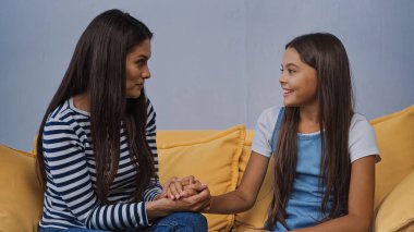 Anne oturma odasında gülümseyen kızıyla el ele tutuşuyor.