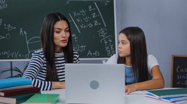 mother and daughter doing homework near laptop and notebooks on table clipart