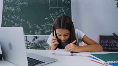 okul çocuğu akıllı telefondan konuşuyor ve dizüstü bilgisayarın yanına yazı yazıyor.