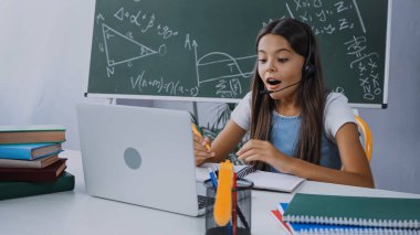 Evde internetten öğrenirken, kulaklık takan heyecanlı çocuk dizüstü bilgisayara bakıyor.