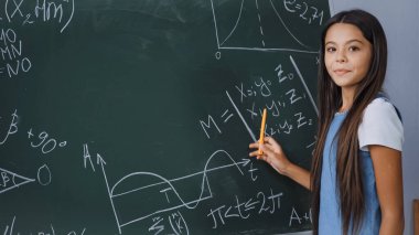 Matematiksel formülleri karatahtada gösterirken elinde kalem tutan çocuk 