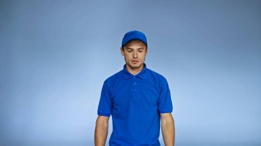 upset delivery man in uniform standing isolated on blue clipart