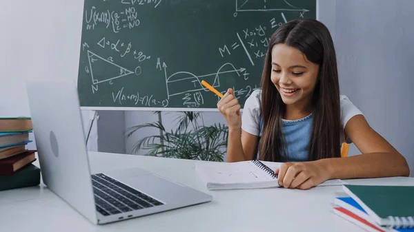 Menina Feliz Segurando Caneta Olhando Para Notepad Perto Laptop Mesa — Fotografia de Stock