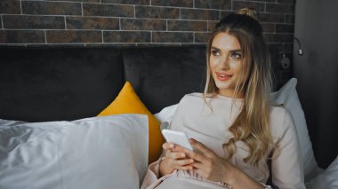 Modern otel odasında akıllı telefondan mesaj atan mutlu genç bir kadın.