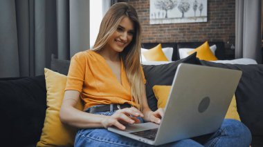 happy freelancer using laptop while sitting on sofa in hotel room  clipart