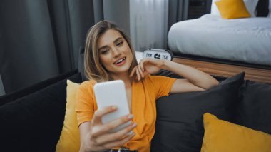 Otel odasındaki kanepede selfie çeken neşeli kadın.