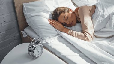 young woman sleeping near alarm clock on bedside table clipart