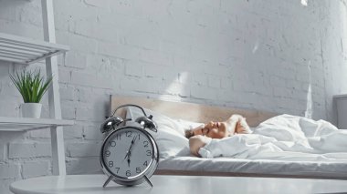 retro alarm clock near sleepy woman lying on bed in morning  clipart
