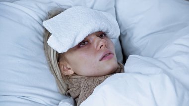 Genç, hasta bir kadın, alnına baskı uygulayarak yatakta yatıyor.