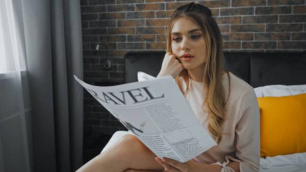 blonde woman reading travel newspaper in hotel room 