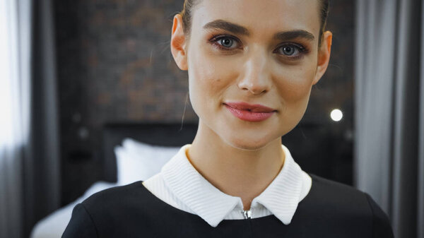 cheerful housekeeper looking at camera in hotel room