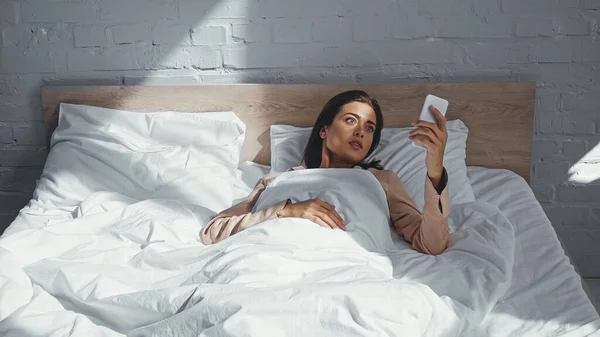 Surprised Woman Looking Smartphone While Lying Bed — Stock Photo, Image