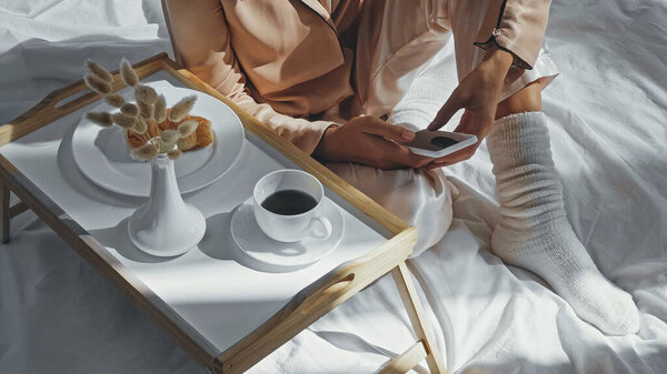 обрезанный вид женщины с помощью смартфона возле лотка с вкусным завтраком и чашкой кофе
