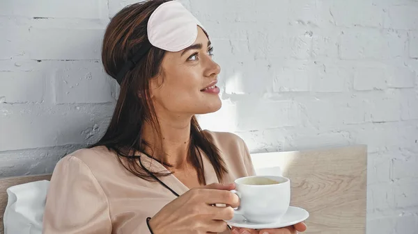 Happy Woman Eye Mask Holding Cup Saucer While Looking Away — Stock Photo, Image