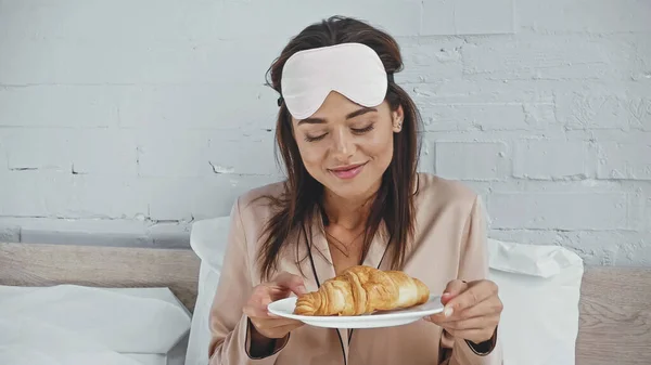 快乐的女人带着眼罩拿着盘子和美味的羊角面包 — 图库照片